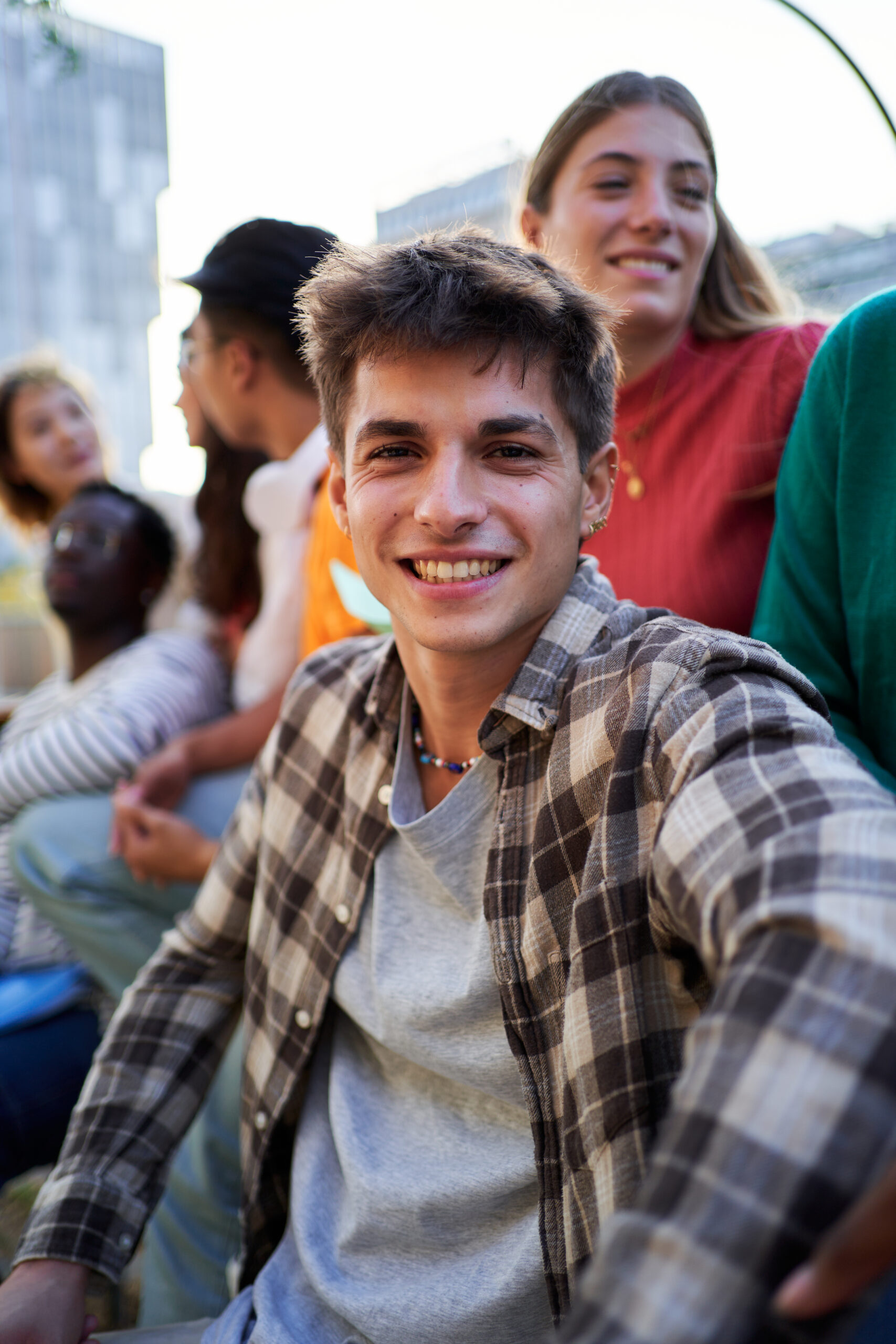 Cheerful vertical portrait of a young caucasian male student looking at camera while sitting outside university gathering with friends.