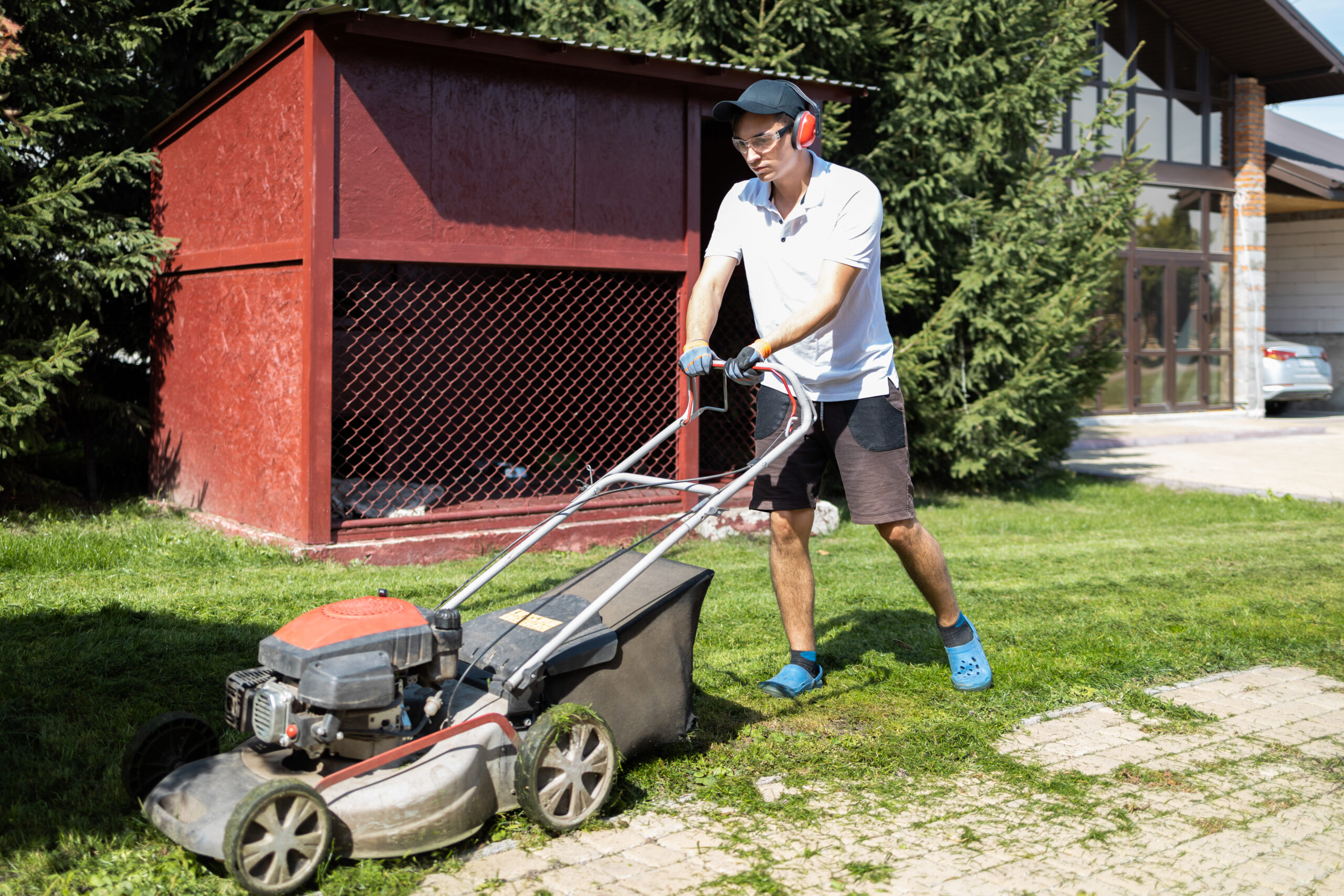 Man in protective headphones and glasses mowing the grass near the house